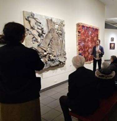 A person explains a piece of art in a gallery to onlookers.